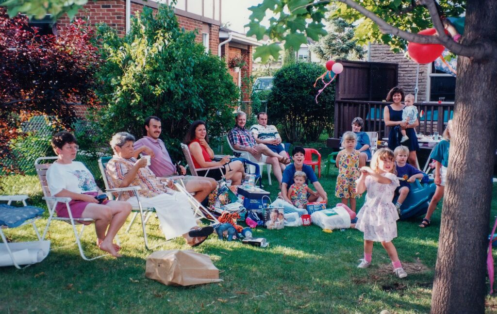 A joyful family gathering outdoors with children playing and adults relaxing in the backyard.