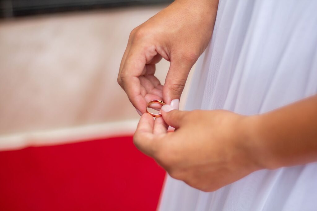 Close-up of a bride holding a gold wedding ring against a red background in Brazil.