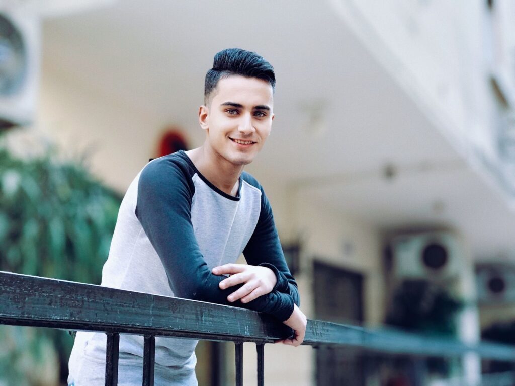 Casual portrait of a smiling young man leaning on a railing outdoors. Happy and relaxed mood.