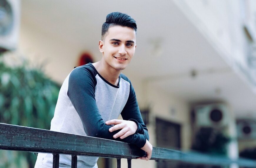 Casual portrait of a smiling young man leaning on a railing outdoors. Happy and relaxed mood.
