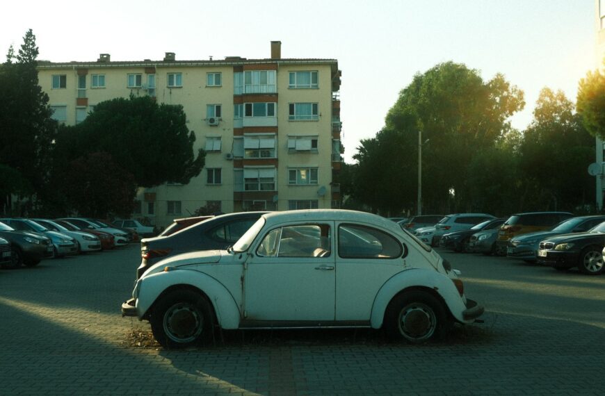 A vintage Volkswagen Beetle parked in an urban residential area with surrounding cars and buildings.