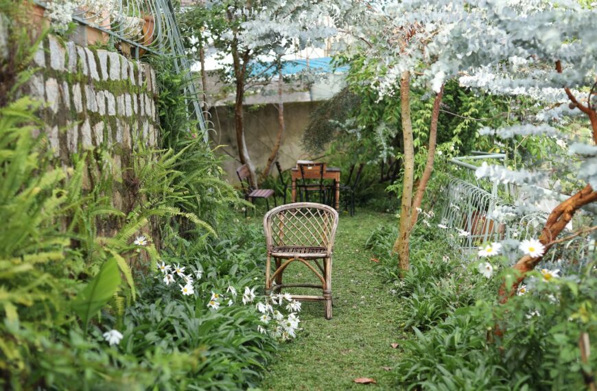 A tranquil garden path with wooden chairs surrounded by lush greenery and flowers.