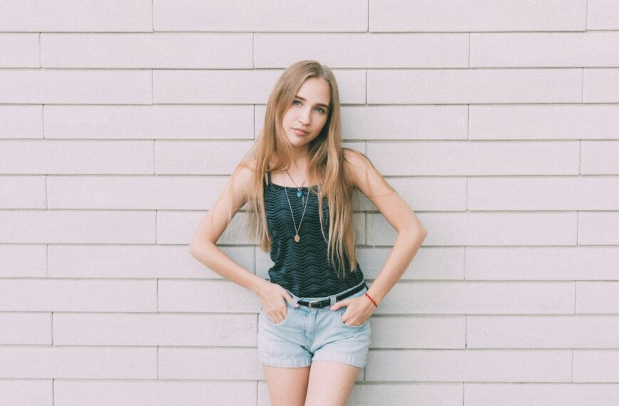 woman in blue denim shorts standing beside white wall