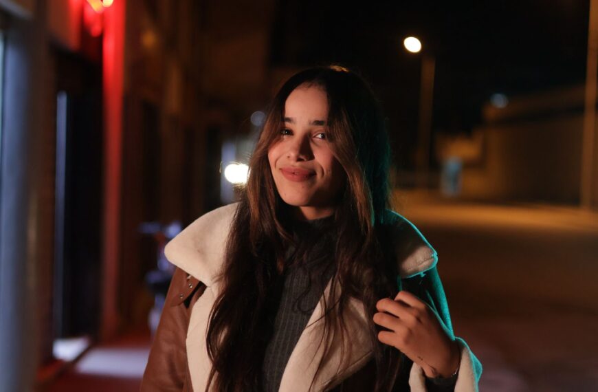 Night portrait of a woman with long hair smiling in an urban setting.