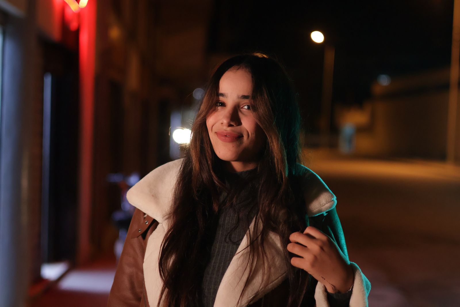 Night portrait of a woman with long hair smiling in an urban setting.