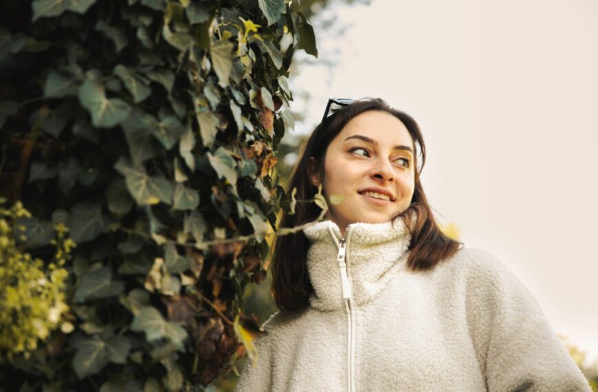 Smiling woman in cozy fleece posed outdoors with lush ivy backdrop.