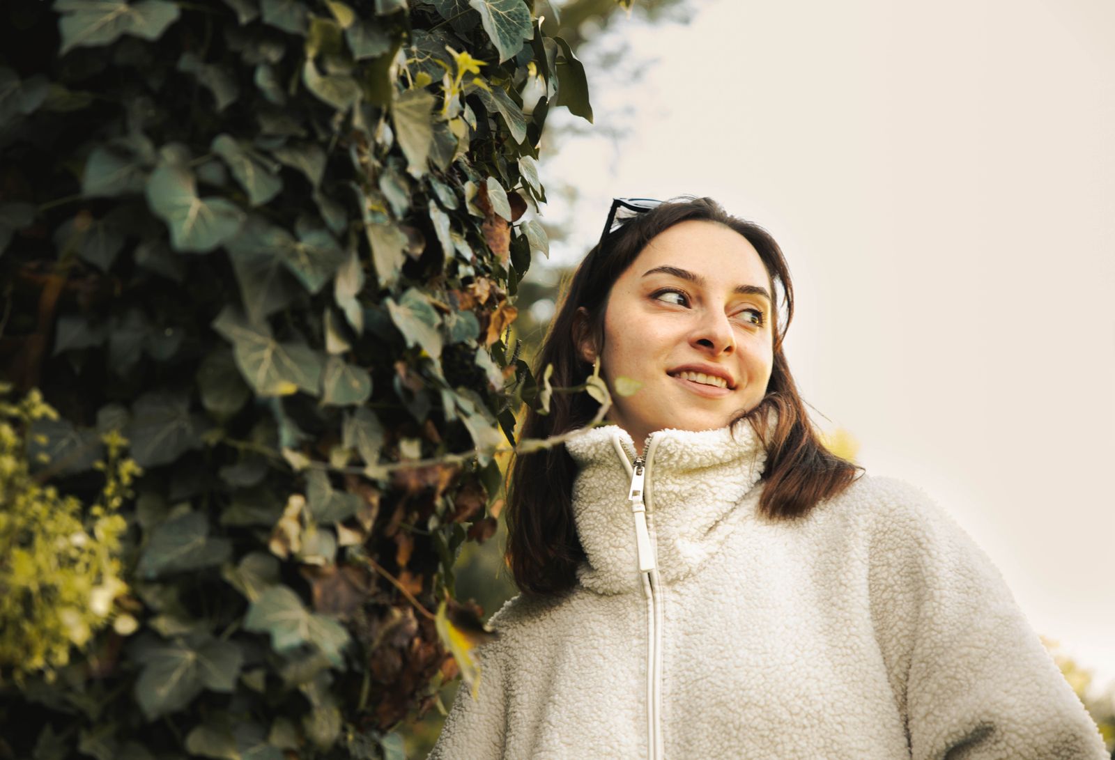 Smiling woman in cozy fleece posed outdoors with lush ivy backdrop.