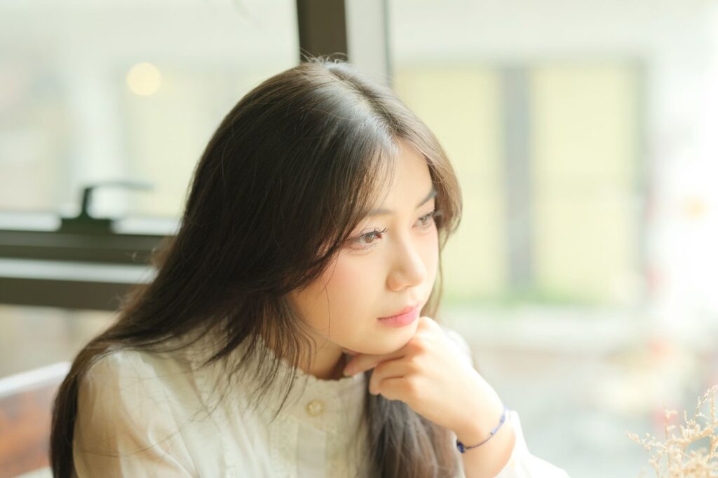 Portrait of a young woman gazing thoughtfully out a window in soft indoor light.