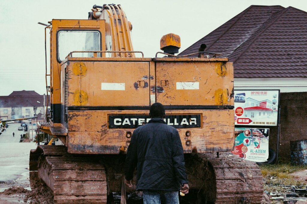 A rugged construction excavator in use behind a worker at a building site.
