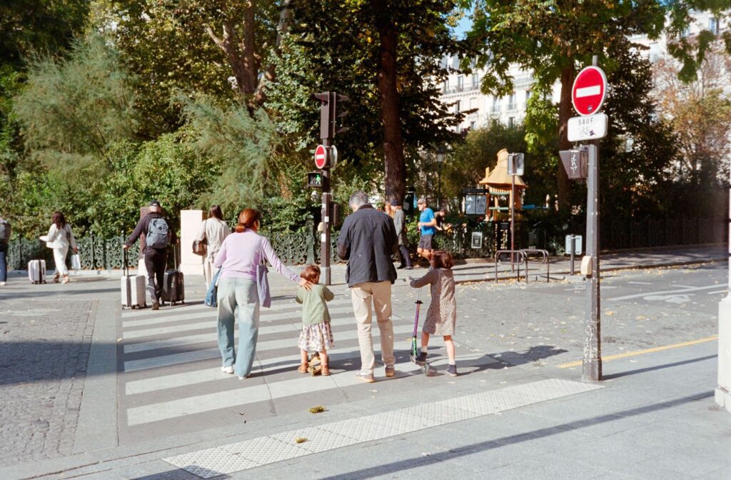 A family crossing the street in Paris on a sunny day, surrounded by greenery.