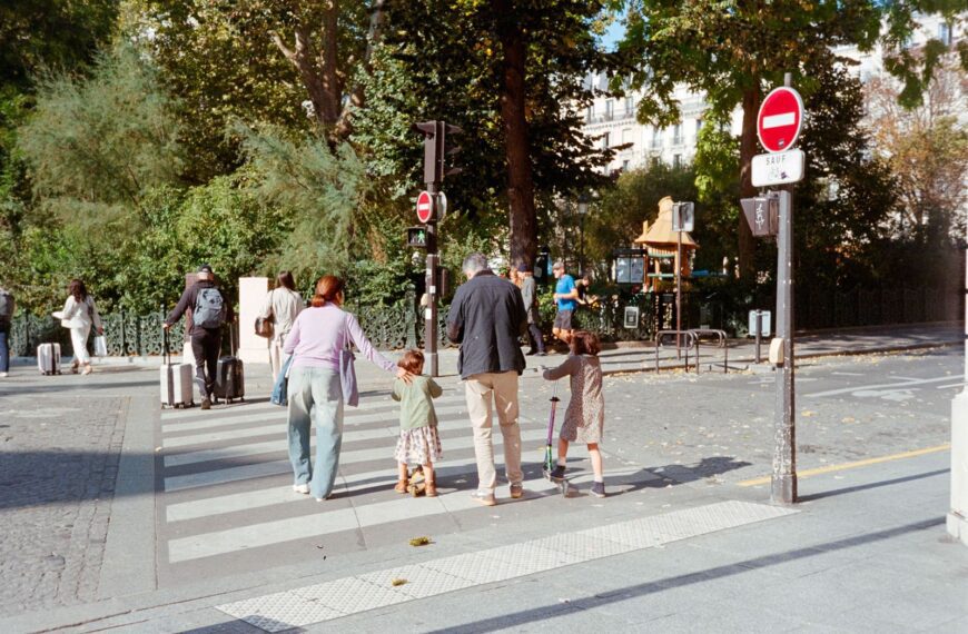 A family crossing the street in Paris on a sunny day, surrounded by greenery.