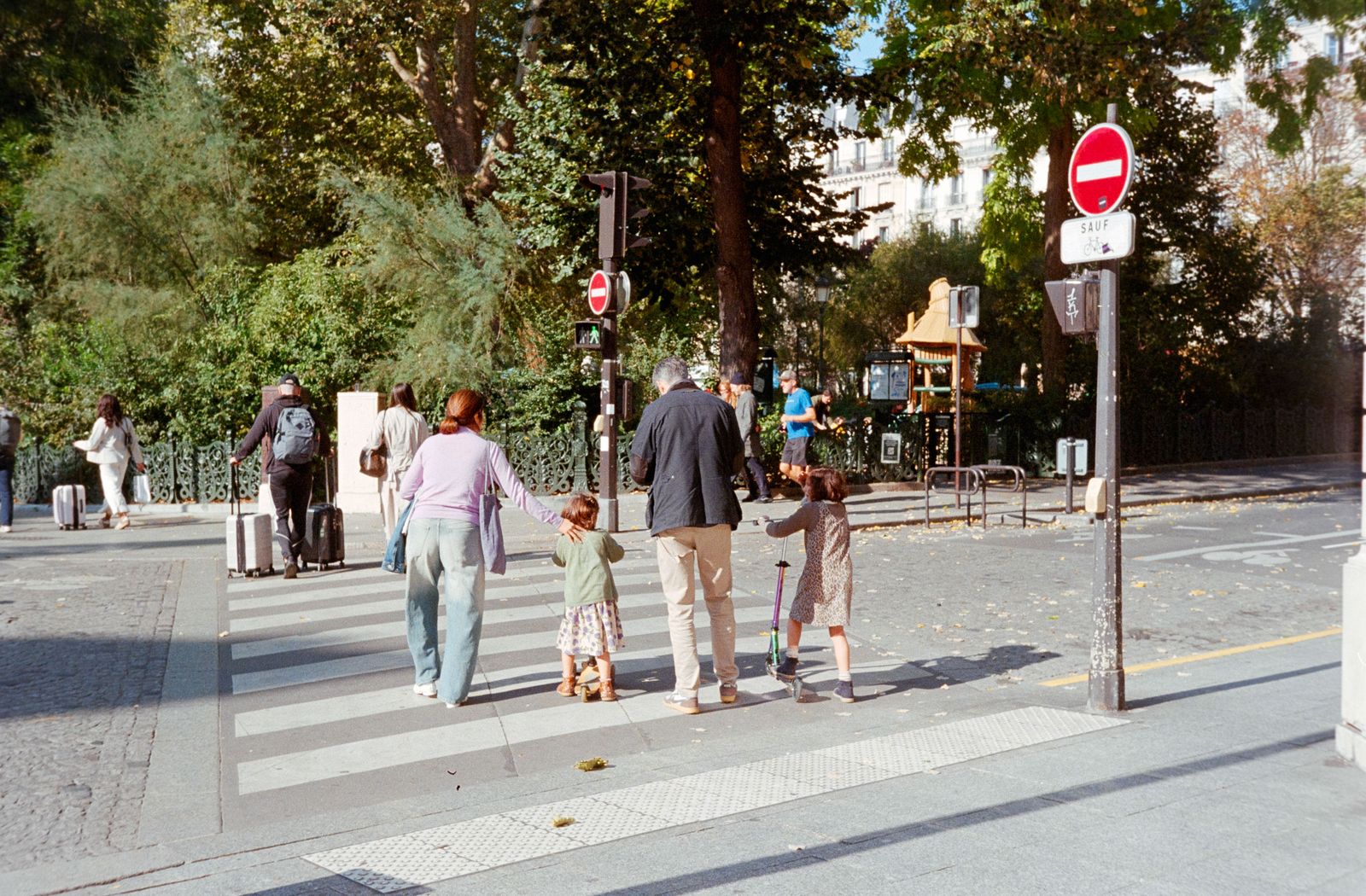 A family crossing the street in Paris on a sunny day, surrounded by greenery.