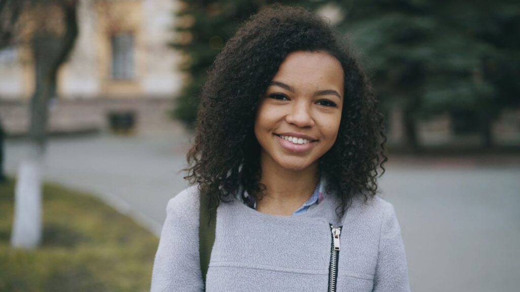 Young woman smiling in an outdoor setting, wearing casual attire.