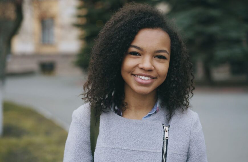 Young woman smiling in an outdoor setting, wearing casual attire.