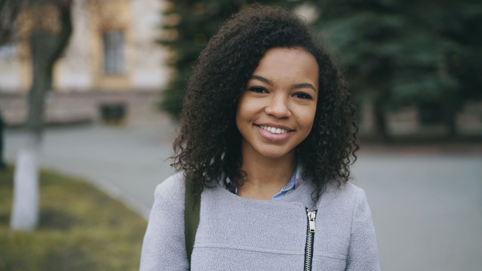 Young woman smiling in an outdoor setting, wearing casual attire.