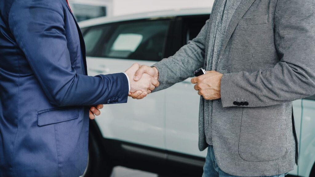 Two businessmen shaking hands in a car dealership, sealing a deal.