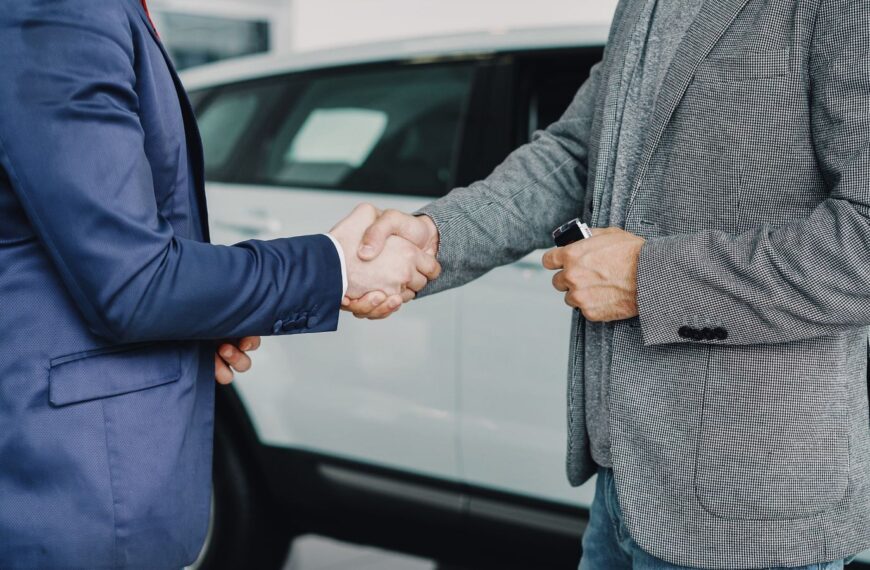 Two businessmen shaking hands in a car dealership, sealing a deal.