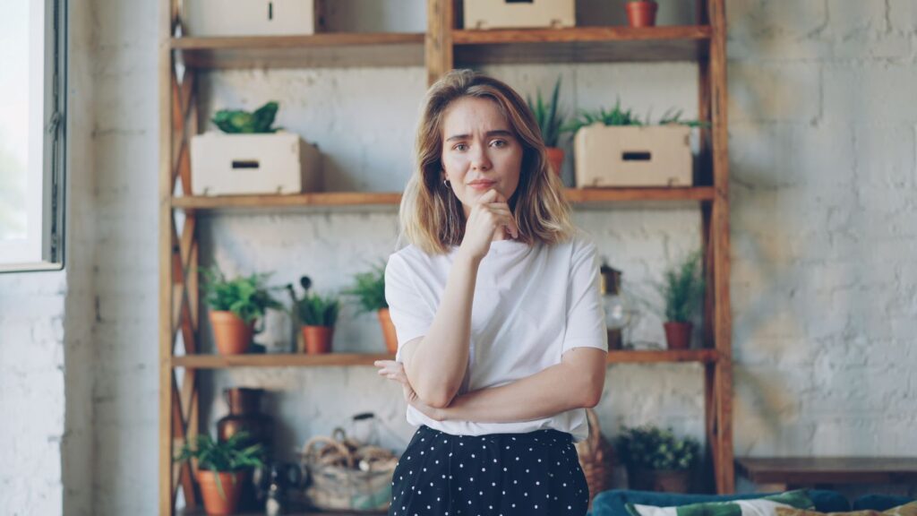 Woman standing thoughtfully in cozy room with plants.