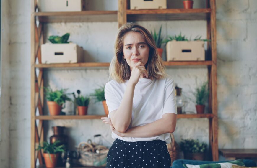 Woman standing thoughtfully in cozy room with plants.
