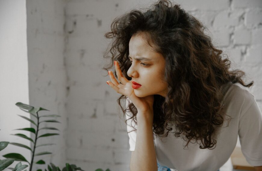 A thoughtful young woman with curly hair indoors, displaying a curious expression.
