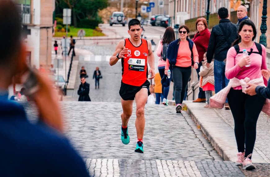 A male athlete runs a marathon through a bustling urban area on a cobblestone street.
