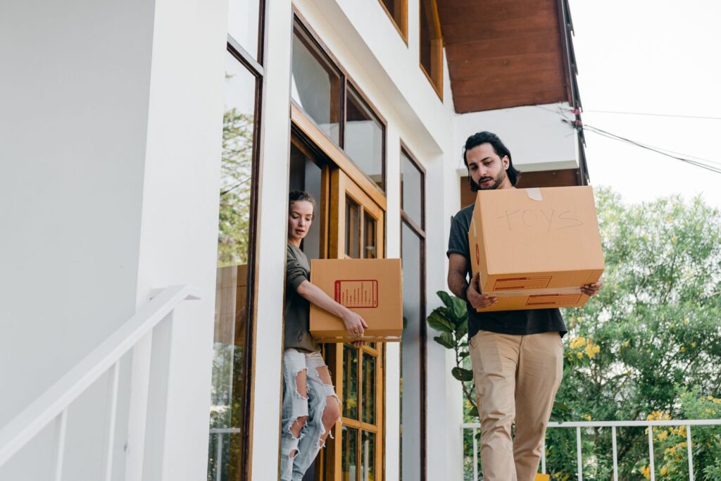 Young diverse male and female in modern casual outfits with cardboard boxes in hands watching step while moving out of old house on summer day
