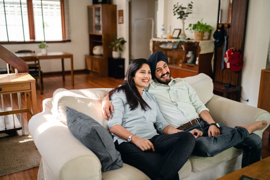From above of cheerful Indian man and woman sitting with crossed legs and cuddling while relaxing together during romantic moment in cozy apartment