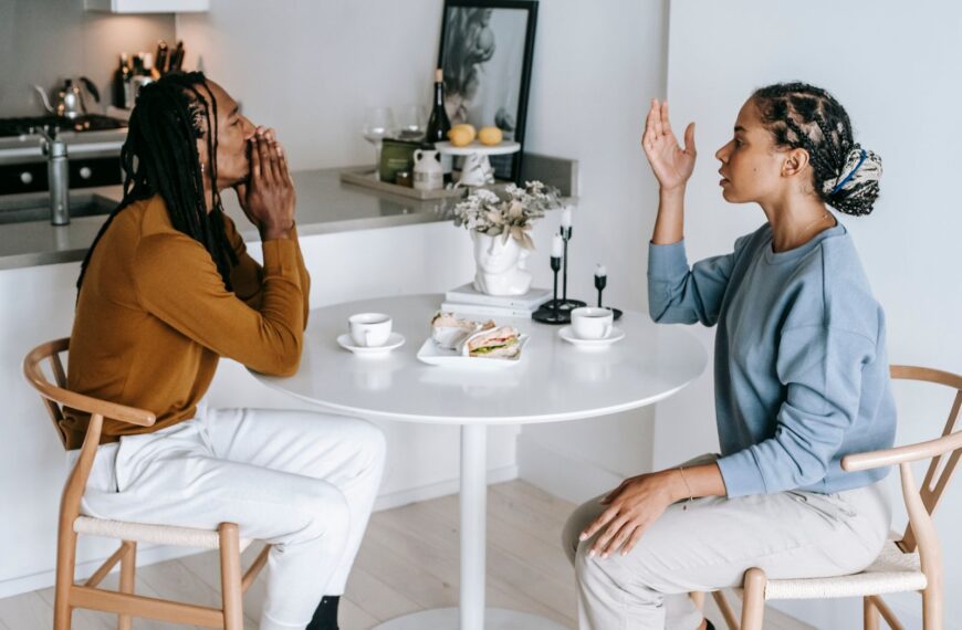 Side view of young African American female sitting at table while arguing with male in casual clothes