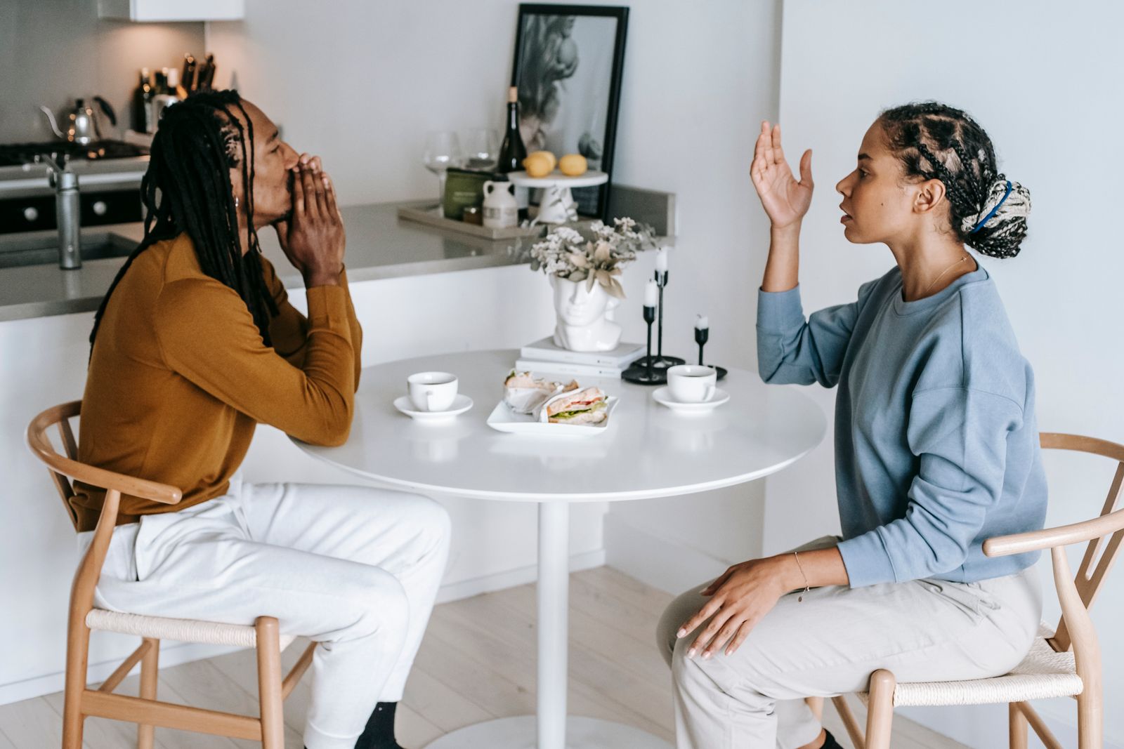 Side view of young African American female sitting at table while arguing with male in casual clothes