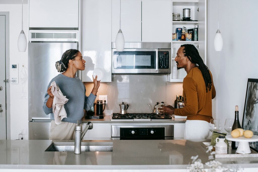 Young black woman talking to annoyed male partner while looking at each other during quarrel in house
