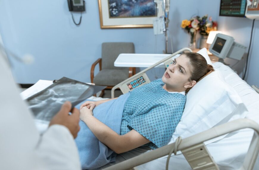Caucasian woman in hospital bed receiving care from healthcare professional.