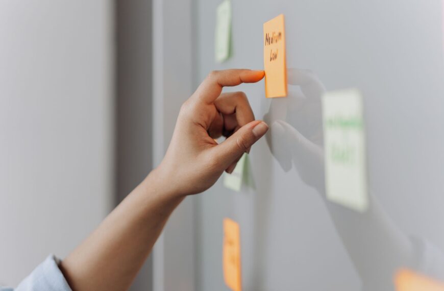A hand placing a sticky note on a reflective surface in an office setting.