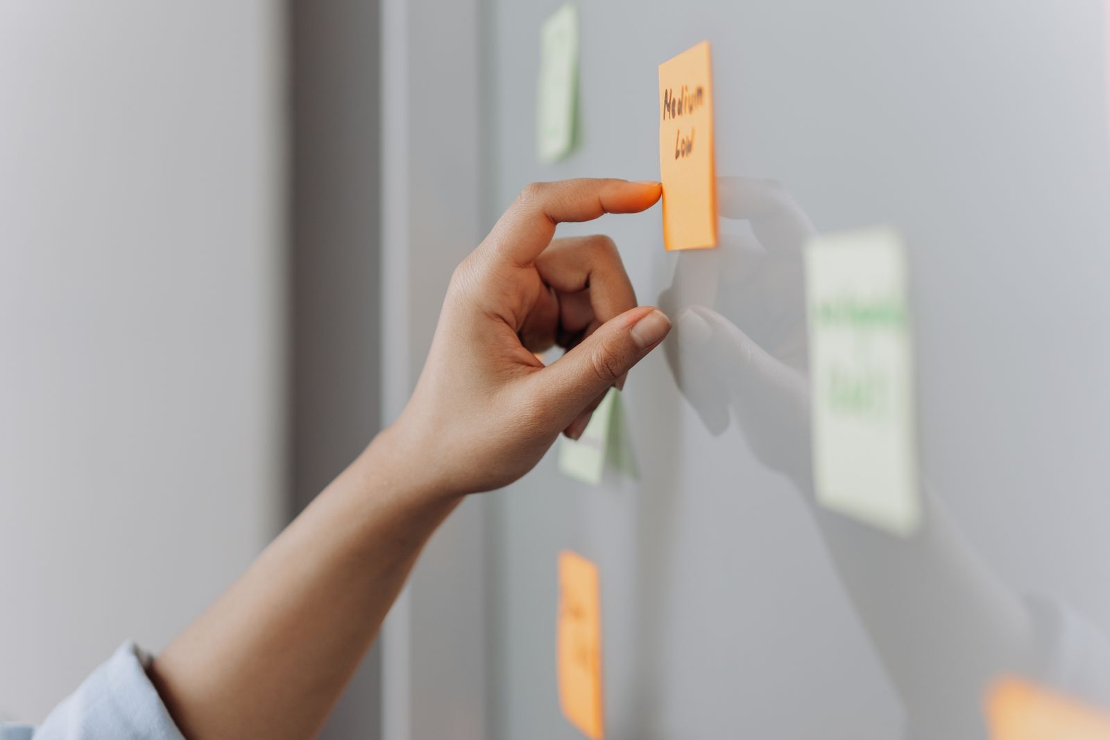 A hand placing a sticky note on a reflective surface in an office setting.