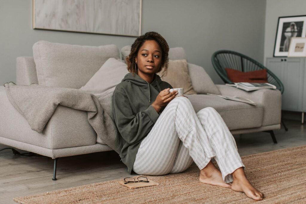 Woman in a gray hoodie drinking coffee while sitting on the floor in a cozy living room.
