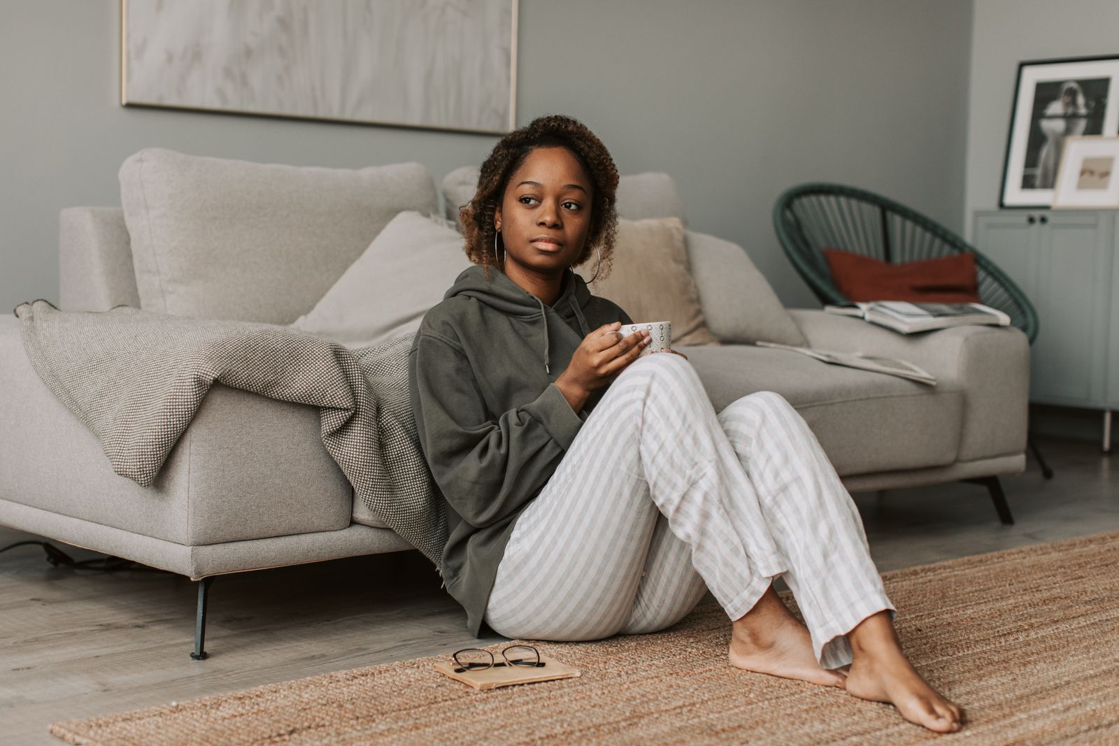 Woman in a gray hoodie drinking coffee while sitting on the floor in a cozy living room.