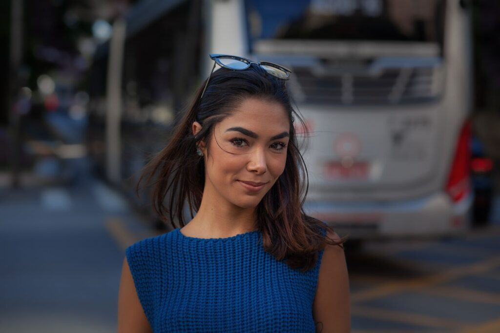 Portrait of a young woman in blue sweater smiling on an urban street.