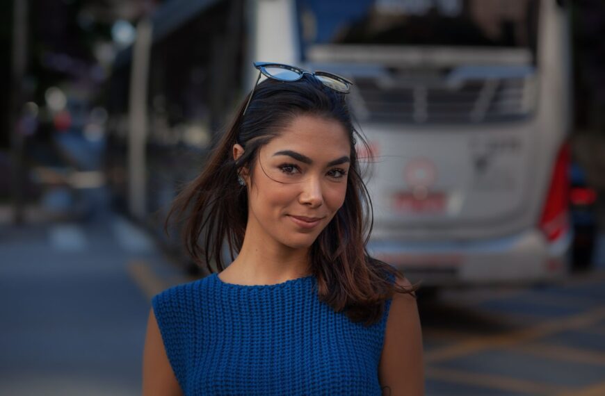 Portrait of a young woman in blue sweater smiling on an urban street.
