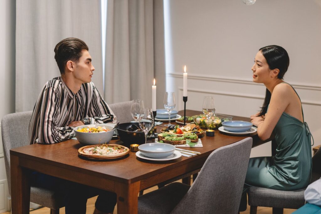 A couple enjoying a candlelit dinner indoors with elegant table settings and gourmet food.