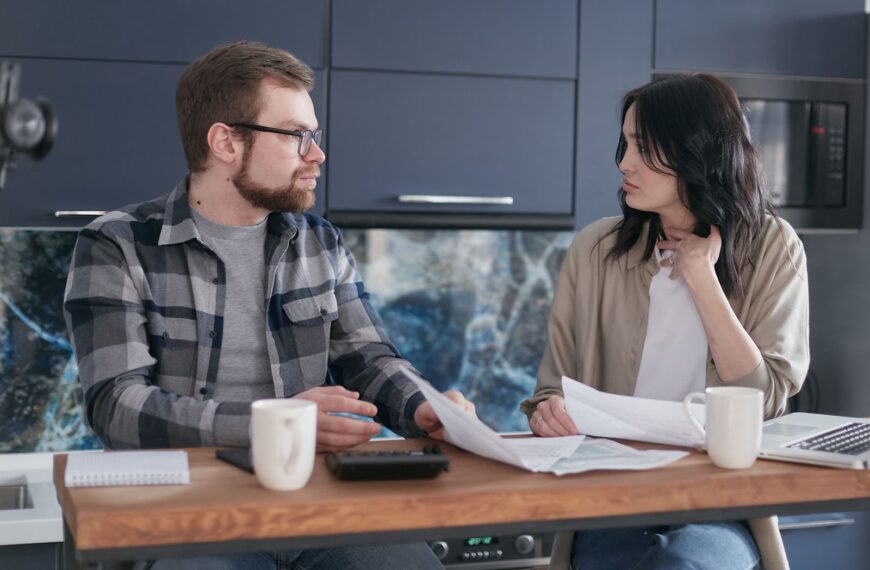 A young couple sitting at a table discussing bills and financial plans in a modern kitchen.