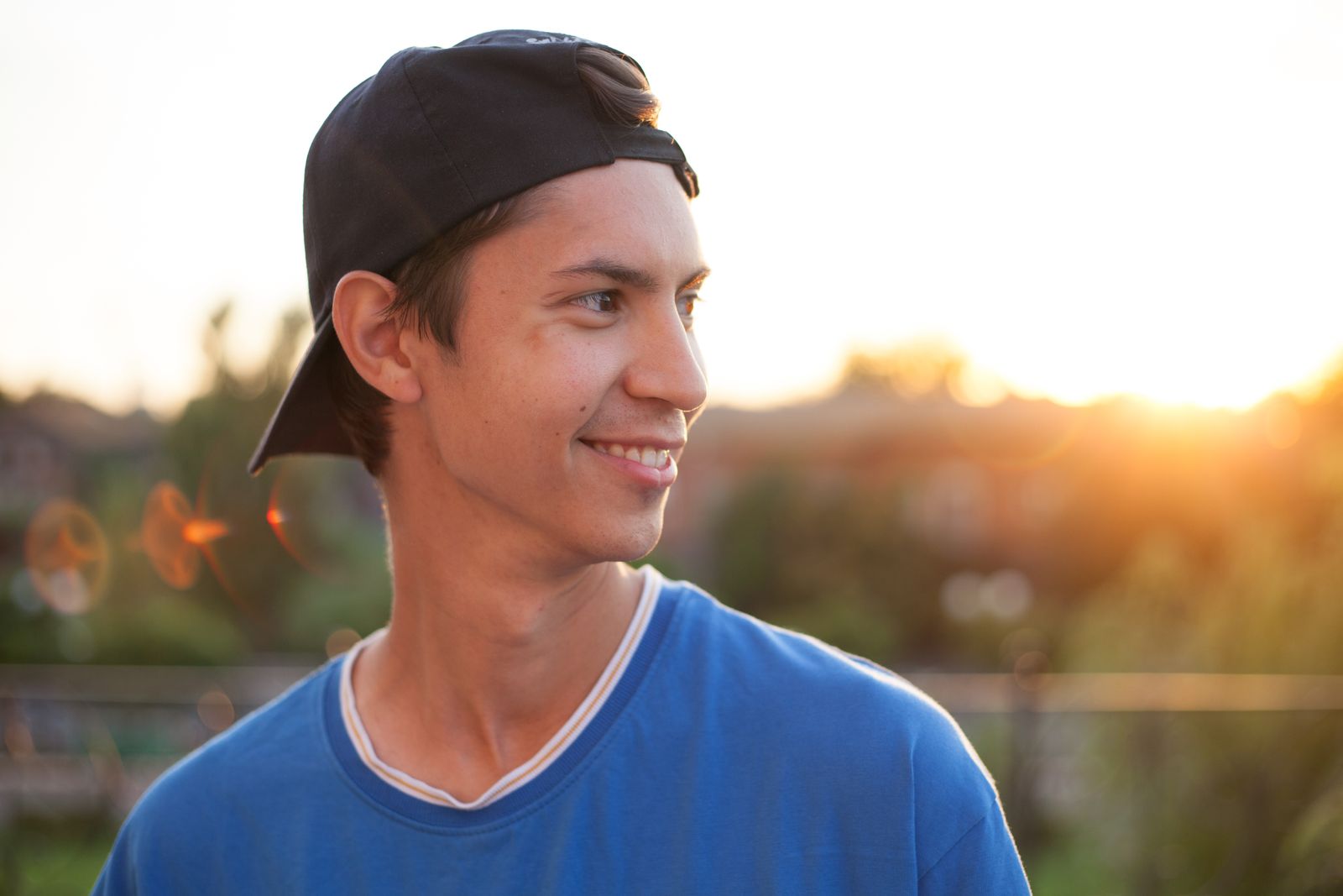 Portrait of a smiling young man in a blue shirt and cap, enjoying a sunset outdoors.