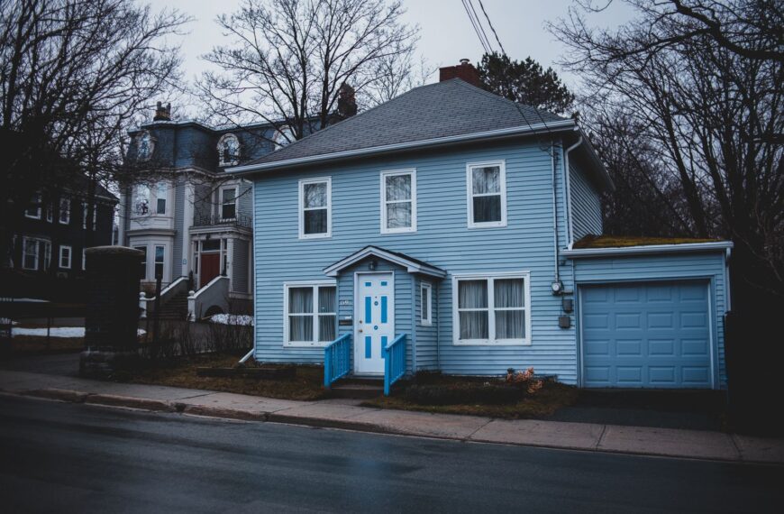 Exterior of small residential house trimmed with light blue wooden panels with white door and adjoin garage
