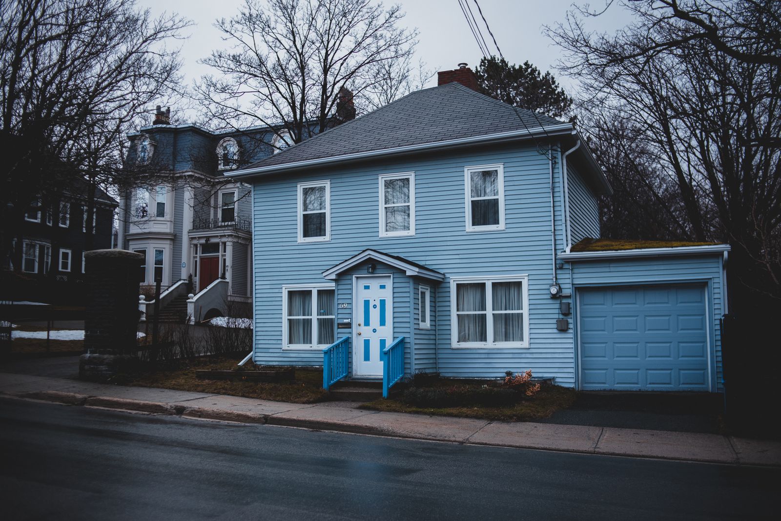 Exterior of small residential house trimmed with light blue wooden panels with white door and adjoin garage