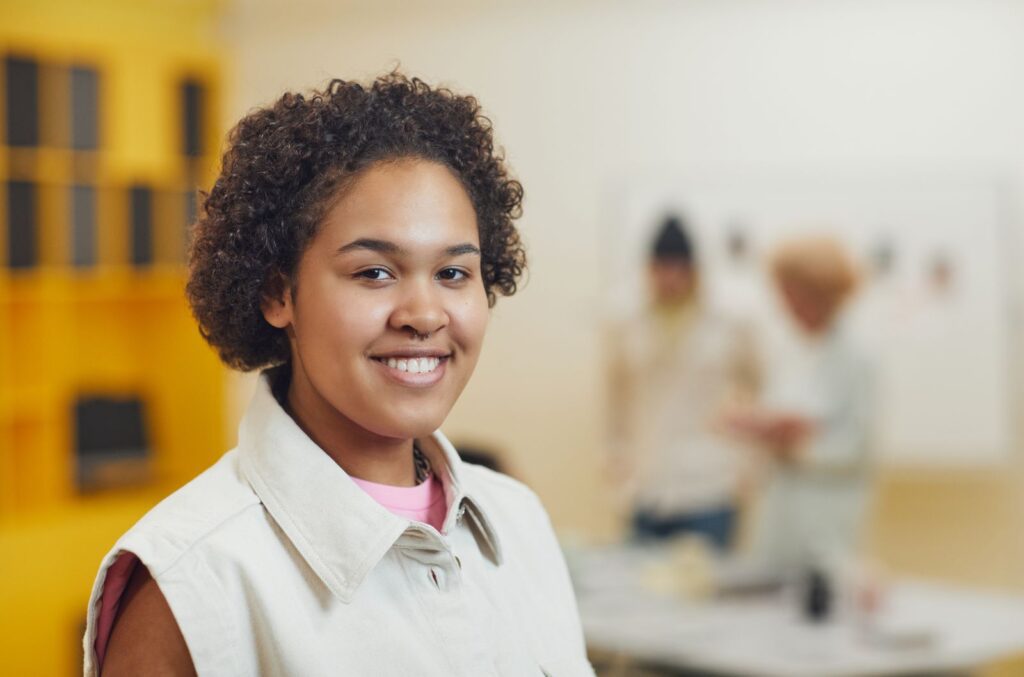 Cheerful young woman with curly hair smiling indoors with a blurred background.