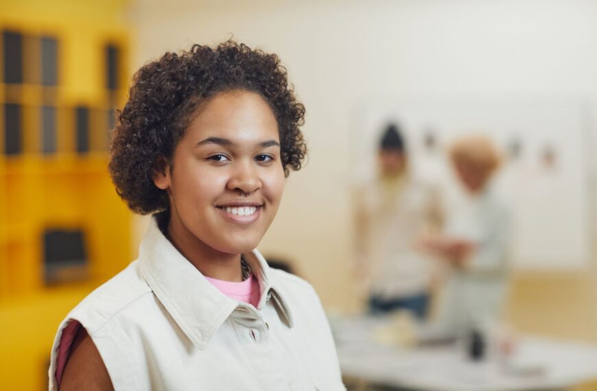 Cheerful young woman with curly hair smiling indoors with a blurred background.