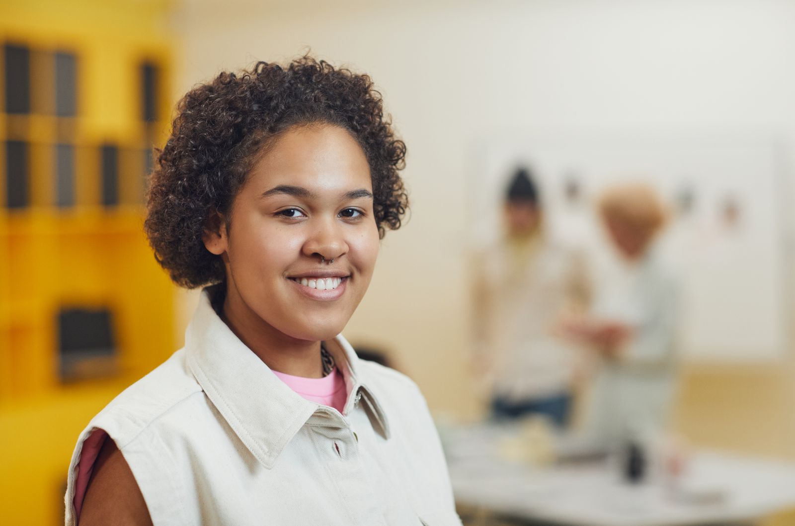 Cheerful young woman with curly hair smiling indoors with a blurred background.