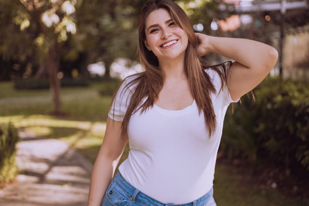 A joyful woman in a white shirt smiles outdoors, embodying confidence and positivity.