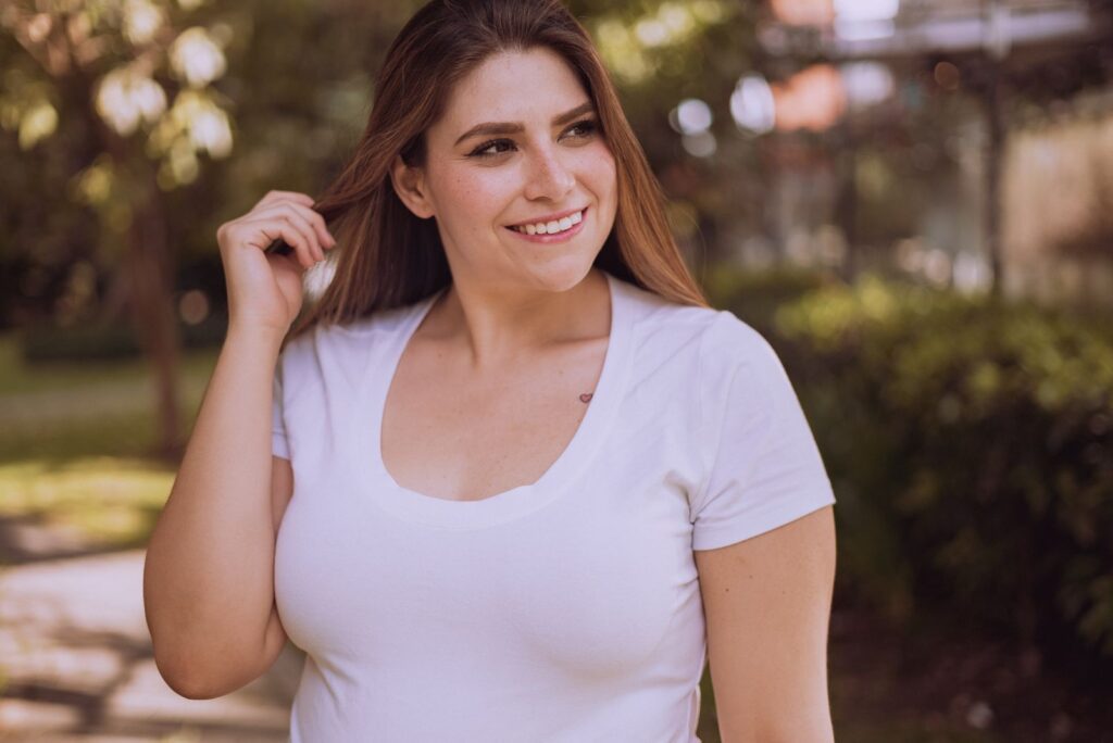 A woman smiles while posing in a white shirt outdoors during the day.