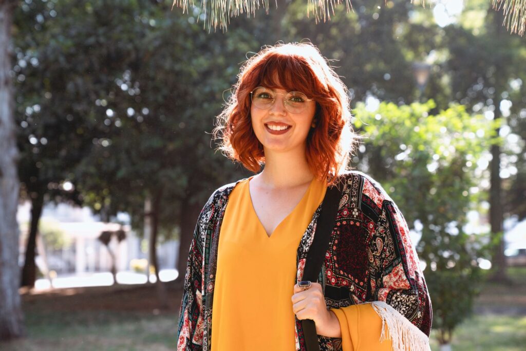 Smiling redheaded woman with glasses enjoying a sunny day outdoors, wearing a colorful shawl.