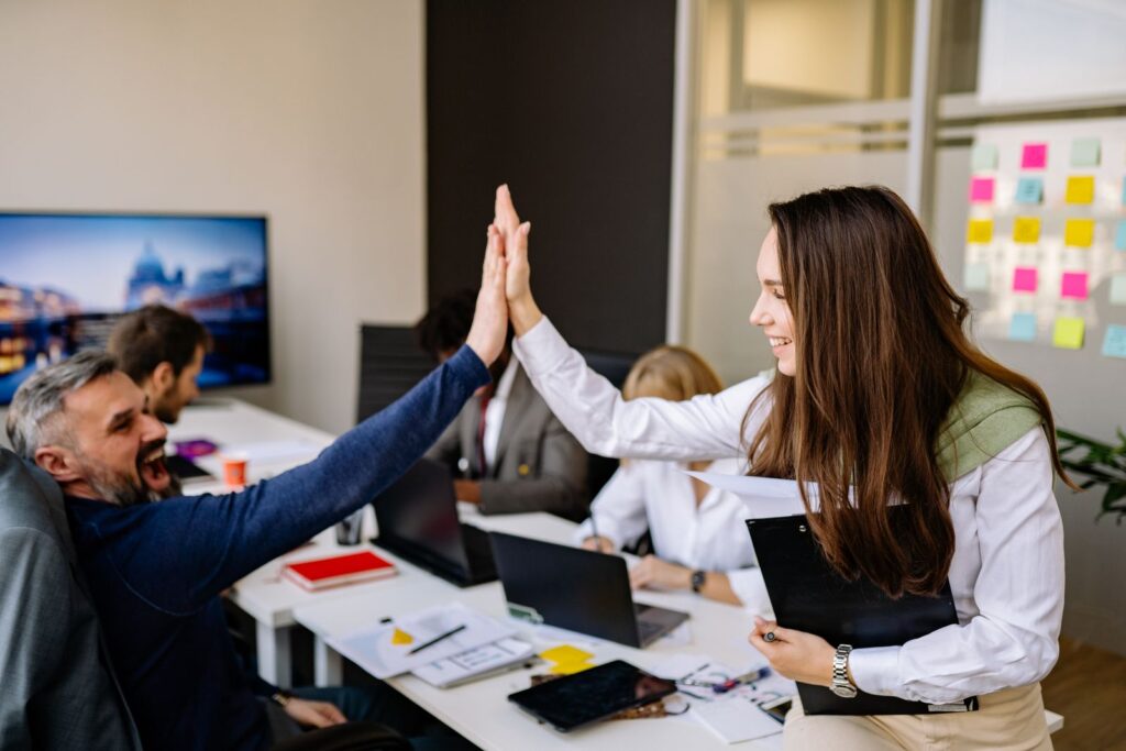 Colleagues in a vibrant office setting high five to celebrate success, conveying teamwork and positivity.