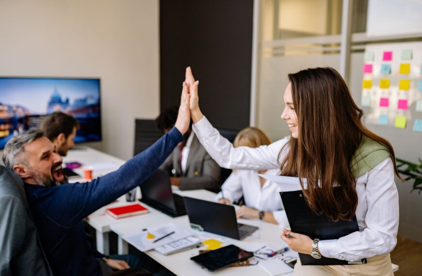 Colleagues in a vibrant office setting high five to celebrate success, conveying teamwork and positivity.